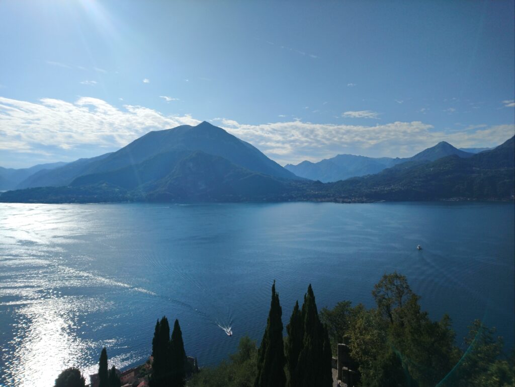 A picture-filling view of a lake with a few trees in the background, two boats on the lake, and mountaneous landscape in the background