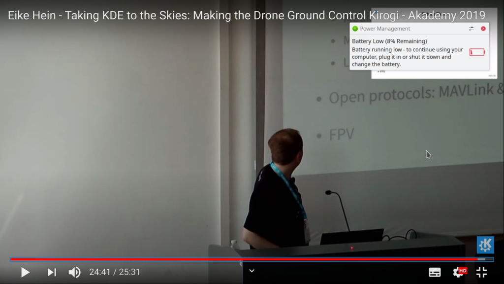 Fullscreen video player of a KDE Akademy 2019 talk “Taking KDE to the Skies: Making the Drone Ground Control Kirogi” with a “Battery running low” notification in the top right